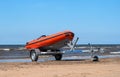 Lifeboat on trailer. The lifeboat is orange. The trailer with the boat is on the shore by the water. Sandy beach Royalty Free Stock Photo