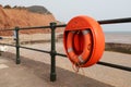 A lifebouy on the railings on Sidmouth Esplanade. The red sandstone Jurassic cliffs can be seen in the background