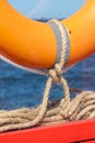 A lifebuoy is attached to a bright orange wooden frame with linen ropes