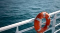 lifebuoy attached to a ship's white railing, with the clear blue sea in the background