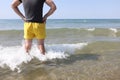 Lifeguard man in yellow shorts stands in sea water and looks into distance