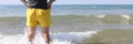 Lifeguard man in yellow shorts stands in sea water and looks into distance