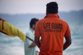 lifeguard in orange shirt carrying flag along the beach with tourists in background at havelock swaraj dweep andaman