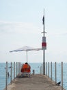 Lifeguard sits in a sun lounger on the pier under an umbrella by the sea on a summer sunny day Royalty Free Stock Photo