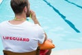 Lifeguard sitting on chair and blowing whistle at poolside Royalty Free Stock Photo