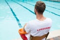 Lifeguard sitting on chair with rescue buoy at poolside Royalty Free Stock Photo
