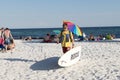 Lifeguard is walking along the beach carrying a rescue surfboard