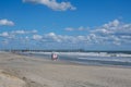 Lifeguard wearing a sweatshirt sitting on a lifeguard stand on a mostly deserted beach with a rough ocean on a cold fall day