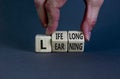 Lifelong learning symbol. Businessman turns wooden cubes with concept words `Lifelong learning` on a beautiful grey background.