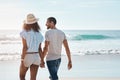 Lifes the best with you by my side. Rearview shot of a young couple walking along the beach.