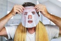 Young scared and surprised man at home using beauty paper facial mask cleansing doing anti aging facial treatment looking himself Royalty Free Stock Photo