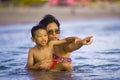 Lifestyle candid portrait of young Asian Indonesian mother and little son enjoying summer holidays having a bath on the sea at Royalty Free Stock Photo