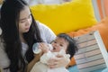 Lifestyle candid portrait of young happy and sweet Asian Japanese woman feeding her beautiful baby girl with formula bottle at Royalty Free Stock Photo