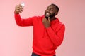 Cheeky cool african american confident bearded guy in red hoodie taking selfie update date app profile photo holding