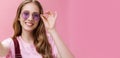 Close-up shot of feminine pretty woman with wavy hair tattoo and small scar on arm touching sunglasses checking frames