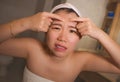 Lifestyle face portrait of young upset and expressive Asian Chinese woman squeezing pimples while looking at the mirror in the Royalty Free Stock Photo