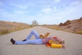 Lifestyle concept of young pretty woman in yellow jacket and blue jeans lying on asphalt empty road with little dog on her with Royalty Free Stock Photo