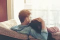 Lifestyle Couple in love and relaxing on a sofa at home and looking outside through the window of the living room, sunny day.