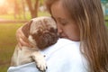 Lifestyle of cute young woman holding pug dog and smiling. Loving dog in his owner`s arms in the park. Concept of caring for a pe Royalty Free Stock Photo