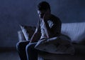 Lifestyle dramatic light portrait of young sad and depressed man sitting at shady home couch in pain and depression feeling stress Royalty Free Stock Photo