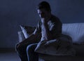 Lifestyle dramatic light portrait of young sad and depressed man sitting at shady home couch in pain and depression feeling lost l Royalty Free Stock Photo