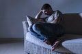 Lifestyle dramatic light portrait of young sad and depressed man sitting at shady home couch in pain and depression feeling lost l Royalty Free Stock Photo