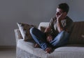 Lifestyle dramatic light portrait of young sad and depressed man sitting at shady home couch in pain and depression feeling lost l Royalty Free Stock Photo