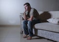 Lifestyle dramatic light portrait of young sad and depressed man sitting at shady home couch in pain and depression feeling lost l Royalty Free Stock Photo