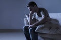 Lifestyle dramatic light portrait of young sad and depressed man sitting at shady home couch in pain and depression feeling lost l Royalty Free Stock Photo