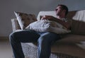 Lifestyle dramatic light portrait of young sad and depressed man sitting at shady home couch in pain and depression feeling lost l Royalty Free Stock Photo