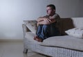 Lifestyle dramatic light portrait of young sad and depressed man sitting at shady home couch in pain and depression feeling stress Royalty Free Stock Photo