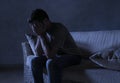 Lifestyle dramatic light portrait of young sad and depressed man sitting at shady home couch in pain and depression feeling stress Royalty Free Stock Photo