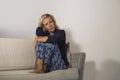 Lifestyle dramatic portrait of attractive and sad woman feeling frustrated and anxious sitting at home sofa couch depressed suffer