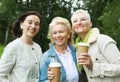 Charming elderly women friends are walking, talking and drinking coffee. Summer day in the park. Royalty Free Stock Photo