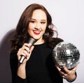 young brunette woman wearing black dress, holding disco ball and singing into microphone Royalty Free Stock Photo