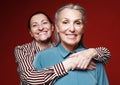 Lifestyle, friendship and old people concept. Two elderly women friends hugging on red background. Royalty Free Stock Photo