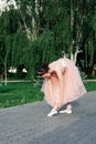 lifestyle full-length portrait of a ballerina in a pink dress with a full organza skirt bends down to her leg to tie