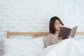 Lifestyle happy young Asian woman enjoying lying on the bed reading book pleasure in casual clothing at home. Royalty Free Stock Photo