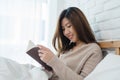 Lifestyle happy young Asian woman enjoying lying on the bed reading book pleasure in casual clothing at home. Royalty Free Stock Photo