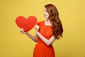 Lifestyle and Holiday Concept - Portrait Young happy red hair woman in orange beautiful dress holding big red heart Royalty Free Stock Photo