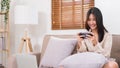 Lifestyle at home concept, Young Asian woman use smartphone to playing games while sitting on sofa Royalty Free Stock Photo