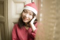 Lifestyle home portrait of young beautiful and happy Asian Korean woman in Santa Claus hat and red jersey enjoying Christmas time Royalty Free Stock Photo