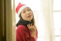 Lifestyle home portrait of young beautiful and happy Asian Korean woman in Santa Claus hat and red jersey enjoying Christmas time Royalty Free Stock Photo