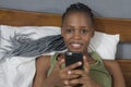 Lifestyle home portrait of young happy and attractive black African American woman lying on bed using social media app in mobile Royalty Free Stock Photo