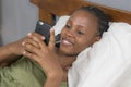 Lifestyle home portrait of young happy and attractive black African American woman lying on bed using social media app in mobile Royalty Free Stock Photo