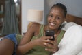 Lifestyle home portrait of young happy and attractive black African American woman lying on bed using social media app in mobile Royalty Free Stock Photo