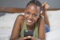 Lifestyle home portrait of young happy and attractive black African American woman lying on bed using social media app in mobile Royalty Free Stock Photo