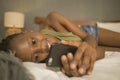 Lifestyle home portrait of young happy and attractive black African American woman lying on bed using social media app in mobile Royalty Free Stock Photo