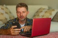 Lifestyle home portrait of young happy and attractive man at home sofa couch working on laptop computer using mobile phone relaxed Royalty Free Stock Photo