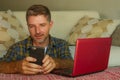 Lifestyle home portrait of young happy and attractive man at home sofa couch working on laptop computer using mobile phone relaxed Royalty Free Stock Photo